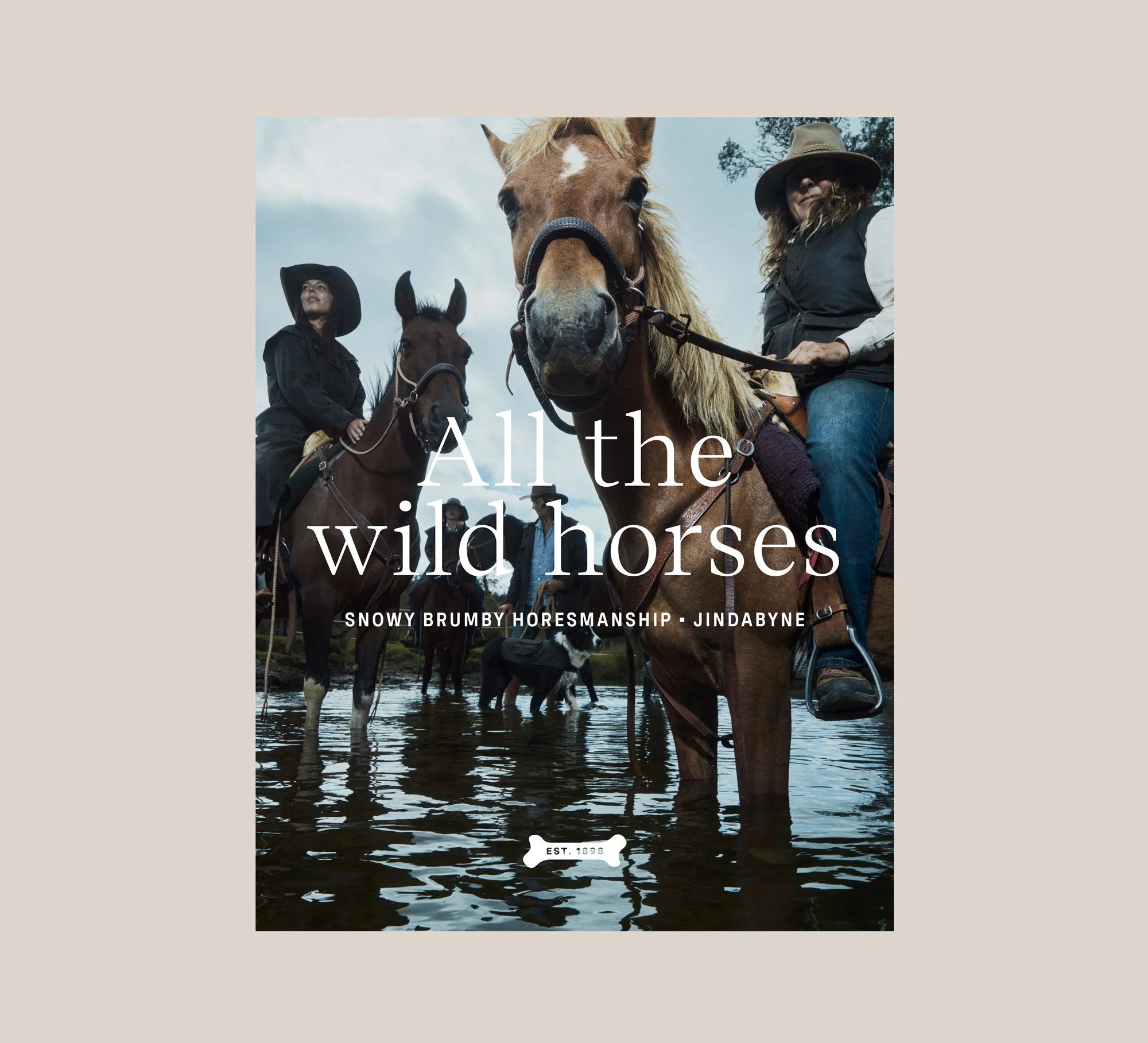 A collection of horses and riders, standing in shallow water, wearing Driza-Bone Heavyweight Heritage Jackets and Vests. Text overlays the image stating "All the wild horses" and "snow brumby horsemanship - Jindabyne".