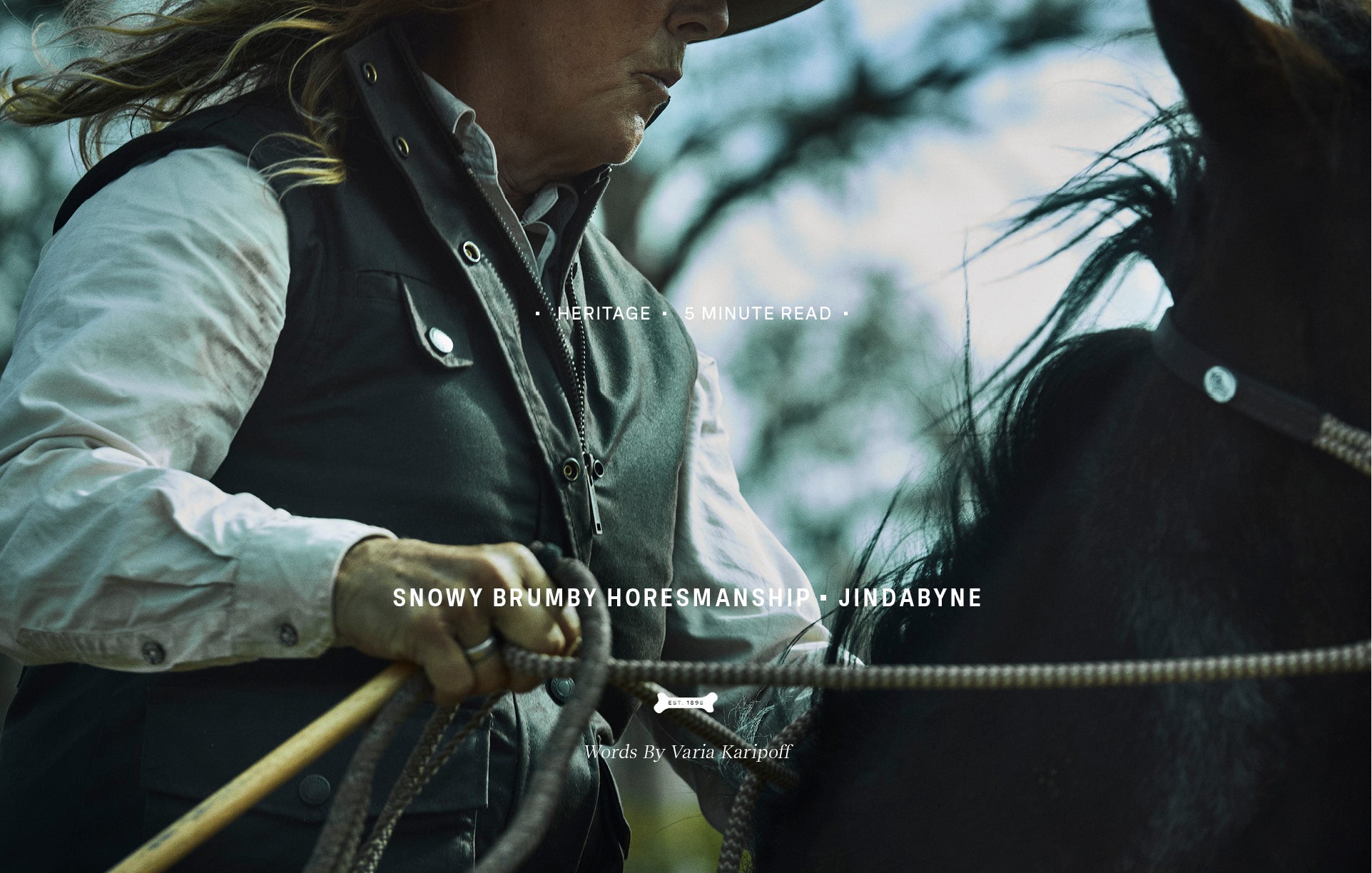 A close-up lifestyle photograph of a person in western attire holding horse reins next to a dark horse, with overlaid text reading 'SNOWY BRUMBY HORESMANSHIP' and 'JINDABYNE' plus a Driza-Bone Dogbone logo at the bottom.