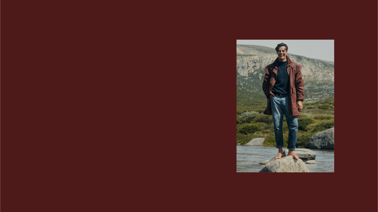 Father's Day 20% Off Sitewide* Promotion. A man stands barefoot on a rock by a river with mountains in the background, wearing a brown leather jacket, dark shirt, and blue jeans, set against a solid dark maroon background.